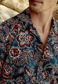 Blumenhemd mit kurzen Ärmeln in Dunkelblau, mit mustern in Rot, Weiß und Grün. Strukturierter Stoff mit einem spitzen Kragen und Knopfdetails.