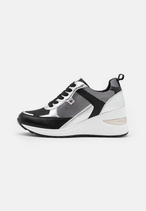Zwart-witte en zilveren plateau sneaker met mesh-panelen, zwarte veters en een lusje aan de hiel, geplaatst op een witte achtergrond.