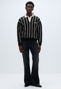 Maglione a righe bianche e nere in maglia con collo a camicia, abbinato a jeans scuri a zampa. Texture morbida, vestibilità casual e dettagli di cuciture visibili.