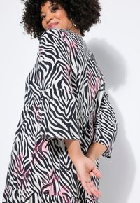 Vestido en blanco y negro con rayas de cebra, mangas acampanadas, tela texturizada y detalles en lentejuelas rosas. Dobladillo ondulante que añade movimiento.