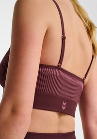 Bordeaux ribbel sportbeha met verstelbare bandjes, voorzien van een textuurdesign en een klein logo op de zoom. De achterkant toont de plaatsing van de bandjes.