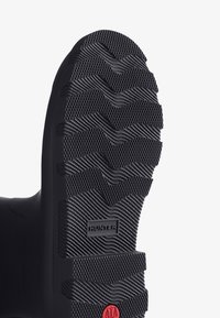 Semelle en caoutchouc noir avec un motif texturé en zigzag pour une meilleure adhérence. Comprend un logo de la marque et un accent rouge.