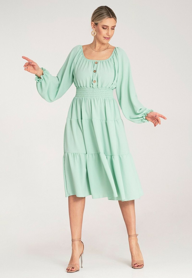Miętowa sukienka z kwadratowym dekoltem, marszczonym pasem w talii, długimi rękawami i falbanistą spódnicą, z guzikami na przodzie.