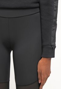 Zwarte sportleggings met een gladde textuur, voorzien van een hoge tailleband en een aansluitend ontwerp. De onderkant heeft een doorschijnend netpaneel.