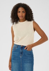 Top sans manches beige en tissu tricoté doux, associé à une jupe en denim bleu taille haute avec poches avant et une légère décoloration.