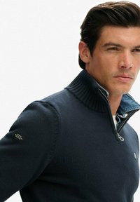 Marineblauer Strickpullover mit geripptem Kragen, Viertel-Reißverschluss-Design, strukturierter Stoff und einem Innenfutter aus Denim am Kragen.