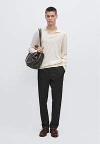 Maglione crema, vestibilità rilassata, scollo a V poco profondo, abbinato a pantaloni neri, scarpe marroni e una grande borsa in pelle grigia scura.