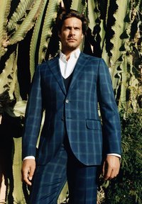 Granatowy, w szachownicę, garnitur z guzikami, nałożony na białą koszulę i czarną kamizelkę. Teksturowany materiał, dopasowany krój, z gładkim wykończeniem kieszeni.