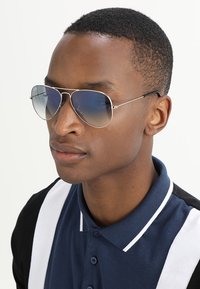 Sunglasses with tinted gradient lenses, silver metal frame, and thin temples. Worn by a person in a blue and white polo shirt.