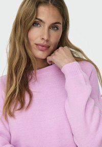 Pull rose clair avec encolure ras du cou côtelée et manches longues, offrant une texture douce et une coupe décontractée. Sans motifs.