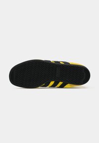 Black and yellow sneaker sole, featuring a textured rubber grip and three distinctive black stripes along the side.