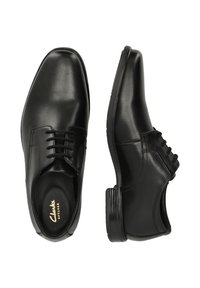 Chaussures formelles noires en cuir avec lacets, l'une montrant une vue de dessus, l'autre en profil latéral, avec la marque "Clarks" sur la semelle intérieure.