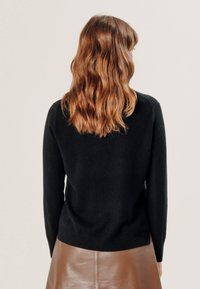 Zwart gebreid sweater met lange mouwen en een geribbelde zoom, gecombineerd met een bruine leren rok. Glide textuur, minimalistisch ontwerp, zichtbare achterkant.