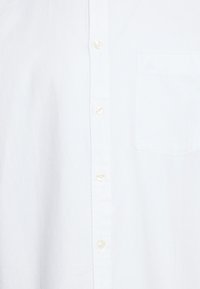 Biała koszula zapinana na guziki, z kieszenią na piersi, wykonana z lekkiego materiału, z zaokrąglonym kołnierzykiem i standardowymi zapięciami na guziki.