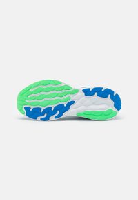 Zool van een sneaker met een witte basis en groene en blauwe rubberaccenten. De textuur bevat een hexagonaal patroon voor grip.