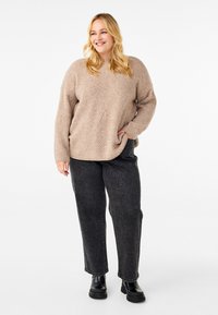 Beżowy sweter z prążkowanej dzianiny o wzorze w diamenty, z długimi rękawami i luźnym krojem, w połączeniu z ciemnoszarymi dżinsami prostymi i czarnymi botkami za kostkę.