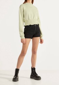 Světle zelená zkrácená mikina se stahovaným spodním lemem, kombinovaná s černými denimovými šortkami a černými šněrovacími bojovými botami. Hladká textura.