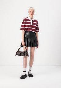 Polo majica prugasta u maroon i bijeloj boji, crna plisirana kožna suknja, mala smeđa torbica, bijele čarape i masivne crne cipele.