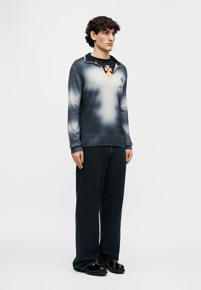 Πλεκτό πουλόβερ σε γκράντιεντ γκρι με γιακά, με γραφικό σχέδιο στο στήθος. Συνδυάζεται με  άνετα σκούρα τζιν και μαύρα παπούτσια.