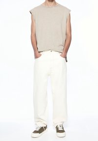 Beige sleeveless shirt, white wide-leg jeans, and two-tone sneakers in olive and white. Simple design and casual fit.
