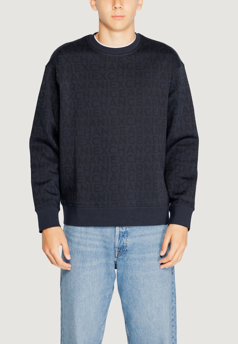 Felpa blu navy con un motivo logo texture, collo a giro, e polsini a costine. Abbinata a jeans denim blu chiaro.
