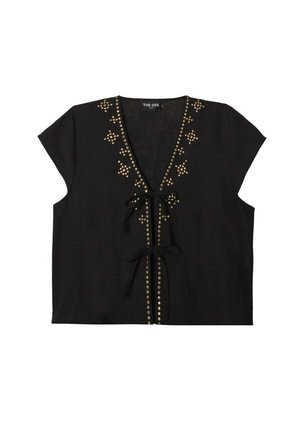 Blusa negra de manga corta con escote en V, tachuelas doradas decorativas en un patrón de diamante y cierre frontal con lazo. Textura similar al lino.