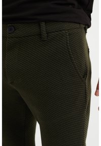 Green patterned pants made of textured fabric, featuring a slim fit, front pockets, and a button closure.