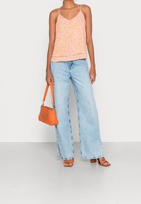 Peachkleurige en oranje patroon camisole met een gelaagd ontwerp, gecombineerd met lichtblauwe wijduitlopende spijkerbroek, oranje handtas en bruine sandalen met blokhak.