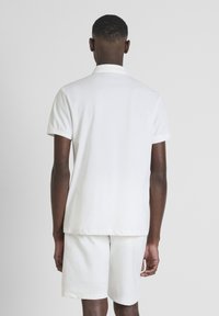 Camisa polo blanca de manga corta, cuello plano y pantalones cortos a juego. Textura suave, sin patrones visibles y ajuste relajado.