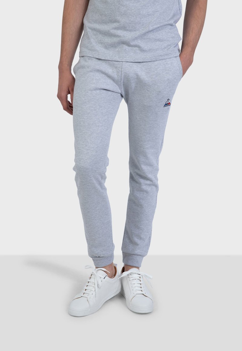 Pantaloni in cotone grigi con gamba affusolata, vita elastica e dettaglio del logo. Abbinati a sneakers bianche. Tessuto morbido, design casual.