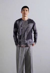 Cămașă din bumbac cu mânecă lungă de culoare gri închis, decorată cu modele mari de frunze de culoare deschisă; asociată cu pantaloni lejeri de culoare gri deschis. Design minimalist.