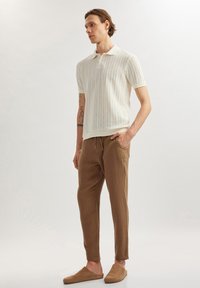 Witte gemarmerde polo met korte mouwen, gecombineerd met losse, bruine broeken en beige instap schoenen. Schone lijnen en een eenvoudig ontwerp.