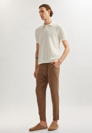 Witte gemarmerde polo met korte mouwen, gecombineerd met losse, bruine broeken en beige instap schoenen. Schone lijnen en een eenvoudig ontwerp.