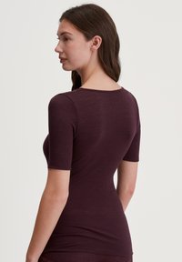 Geribde bordeauxrode top met een ronde halslijn en korte mouwen, voorzien van een getailleerde pasvorm en subtiele textuur.