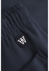 Navy blue, cotton blend joggers featuring a ribbed waistband and a round embroidered logo in white. Includes side pockets. Smooth texture.