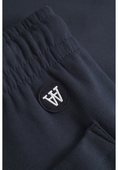 Jogging en mélange de coton bleu marine avec une taille côtelée et un logo rond brodé en blanc. Comprend des poches latérales. Texture lisse.