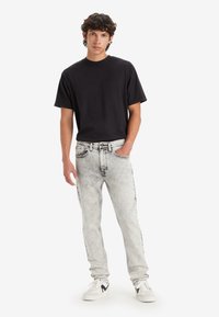 Black short-sleeve t-shirt, light grey faded jeans with black accents, worn with white sneakers. The fit is relaxed, featuring classic denim styling.
