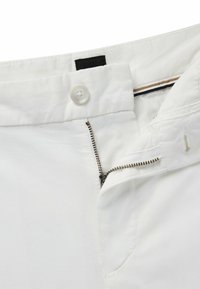 White cotton trousers featuring a button closure, zip fly, and contrasting inner waistband details. Smooth texture with a tailored fit.