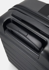 Svart hardcase-koffert med teksturerte vertikale striper, et uttrekkbart håndtak og glidelås som går langs den øverste kanten.