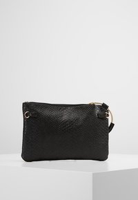 Mustakuvioinen clutch-laukku tekonahasta, jossa on vetoketjukiinnitys, kultaiset yksityiskohdat ja irrotettava hihna.