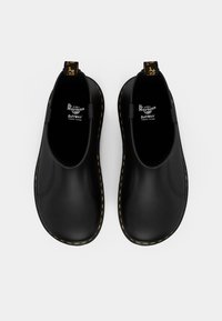 Čierne slip-on topánky s hladkým povrchom, s žltým prešívaním pozdĺž podrážky a s pútkom s logom na päte.
