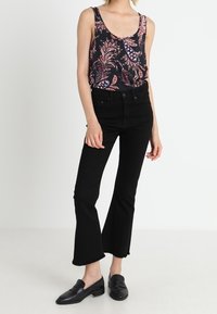 Black floral tank top with a scoop neckline, paired with high-waisted black flared jeans. Black slip-on shoes complete the outfit.