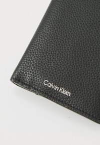 Fekete textúrájú bőr pénztárca ezüst "Calvin Klein" márkázással. Rendentetű felülettel és lekerekített szélekkel rendelkezik. Kompakt méret.