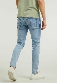 Vaqueros slim fit de color azul claro con un lavado desvanecido, que presentan bolsillos traseros con costuras angulares y un aspecto envejecido, combinados con zapatillas blancas.
