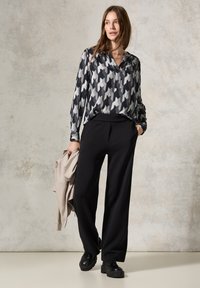 Blusa a righe nera e grigia con scollo a V, abbinata a pantaloni neri a vita alta e scarpe nere chunky. Giacca leggera in mano.