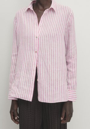 Person wearing a long-sleeve button-up shirt with vertical pink stripes and black textured pants against a plain light background.