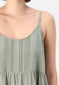 Ανοιχτό πράσινο αμάνικο μπλουζάκι με στρογγυλή λαιμόκοψη, διαθέτει κάθετες δαντελωτές λεπτομέρειες και χαλαρή σιλουέτα με συ�γκεντρωμένη υφή.