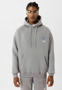 Grijze hoodie met een voorzak, capuchon met trekkoord en blauwe grafische accenten op de borst; gecombineerd met bijpassende grijze broek.
