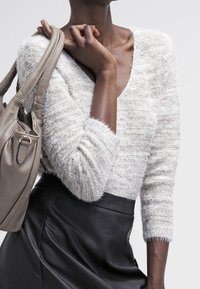 Jasnoszary sweter o teksturowanej fakturze z głębokim dekoltem w kształcie V i luźnym fasonem, w połączeniu z czarną skórzaną spódnicą z wysokim stanem oraz beżową torebką.