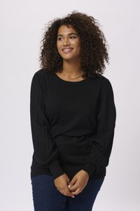 Pull noir avec des manches côtelées, un col rond et une taille ajustée. Texture lisse avec de longues manches bouffantes. Associé à un jean bleu.